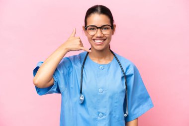Young nurse Colombian woman isolated on pink background making phone gesture. Call me back sign