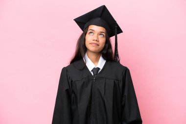 Young university Colombian woman graduate isolated on pink background and looking up