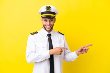 Kafkasyalı pilot sarı arka planda izole edilmiş, şaşırmış ve işaret ediyor.