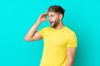 Mavi arka planda mahsur kalmış yakışıklı, beyaz bir adam.