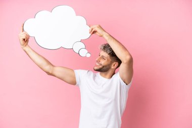 Pembe arka planda izole edilmiş yakışıklı beyaz bir adam düşünce balonu tutuyor.