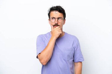 Bıyıklı genç adam beyaz arka planda izole edilmiş, kuşkuları var ve kafası karışmış bir yüz ifadesi var.
