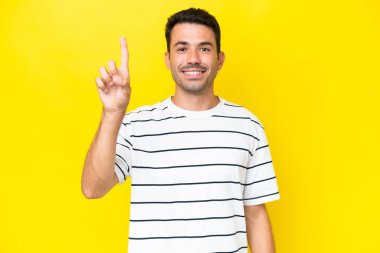 Soyutlanmış sarı arka planı olan yakışıklı genç adam harika bir fikre işaret ediyor.