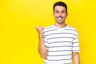 Soyutlanmış sarı arka planda genç yakışıklı bir adam bir ürün sunmak için kenarı işaret ediyor.