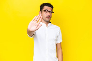 Soyutlanmış sarı arka planda genç yakışıklı adam dur hareketi yapıyor ve hayal kırıklığına uğruyor.