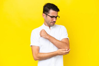 Genç, yakışıklı, soyutlanmış, sarı arka planda, dirseğinde ağrı olan bir adam.