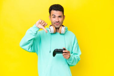 Young handsome man playing with a video game controller over isolated wall showing thumb down with negative expression