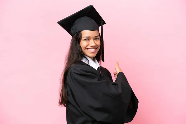Young university Colombian woman graduate isolated on pink background pointing back