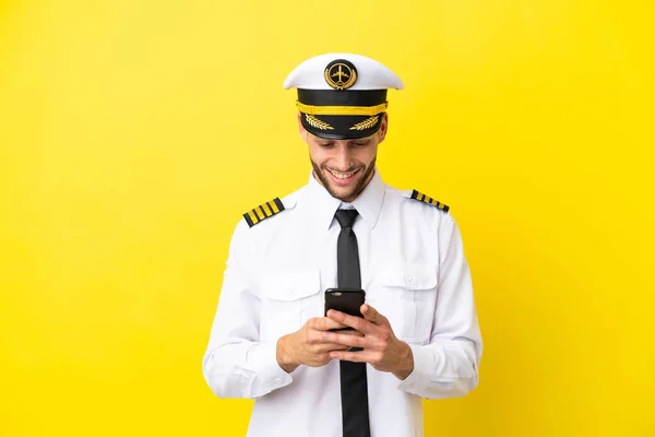 stock image Airplane caucasian pilot isolated on yellow background sending a message with the mobile