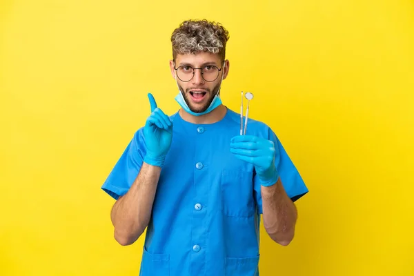 Dentysta Kaukaski Mężczyzna Trzyma Narzędzia Izolowane Żółtym Tle Zamierzając Zrealizować — Zdjęcie stockowe