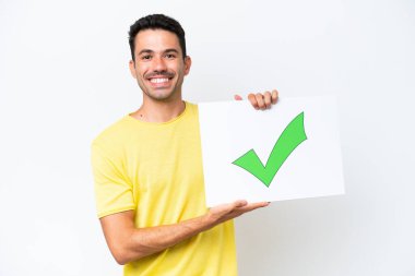 Young handsome man over isolated white background holding a placard with text Green check mark icon with happy expression