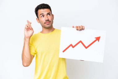 Young handsome man over isolated white background holding a sign with a growing statistics arrow symbol with fingers crossing