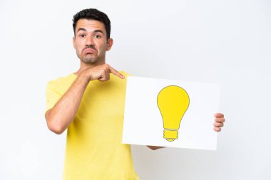 İzole edilmiş beyaz arka planda genç yakışıklı bir adam elinde ampul simgesi olan bir pankart tutuyor ve ona doğrultuyor.