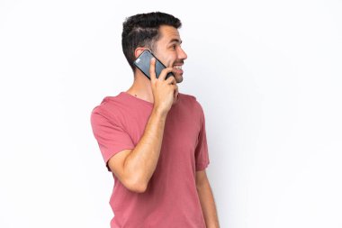 Soyutlanmış beyaz arka planda genç yakışıklı bir adam cep telefonuyla sohbet ediyor.