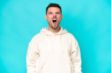 Beyaz tenli yakışıklı adam mavi arka planda izole edilmiş ve ağzı açık bağırıyor.