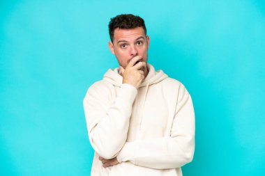 Mavi arka planda izole edilmiş beyaz, yakışıklı genç adam sağa bakarken şaşırmış ve şok olmuştu.