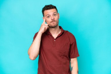 Kafkasyalı yakışıklı genç bir adam mavi arka planda izole edilmiş bir fikir düşünüyor.