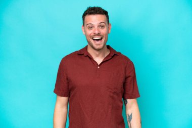 Mavi arka planda yalıtılmış beyaz, yakışıklı, şaşırtıcı bir yüz ifadesi olan genç adam.