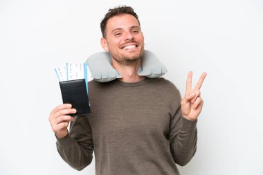 Young caucasian man holding a passport isolated on white background smiling and showing victory sign