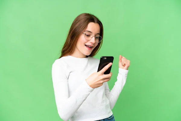 Teenager girl over isolated chroma key background with phone in victory position