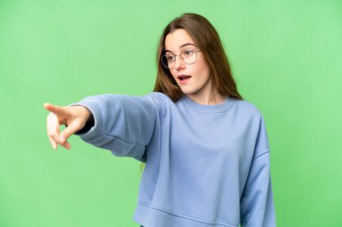 Teenager girl over isolated chroma key background pointing away