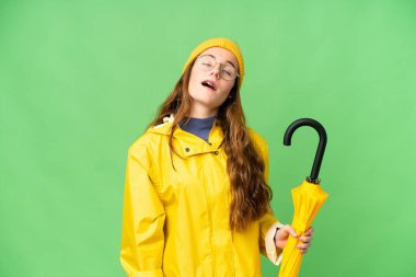 Teenager girl with rainproof coat and umbrella over isolated chroma key background laughing