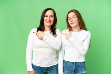 mother and daughter over isolated chroma key background pointing finger to the side and presenting a product