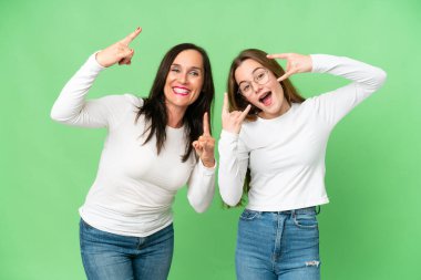 mother and daughter over isolated chroma key background making rock gesture