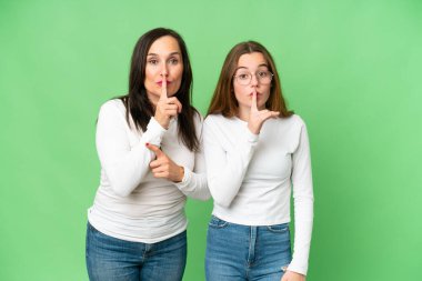 mother and daughter over isolated chroma key background showing a sign of closing mouth and silence gesture