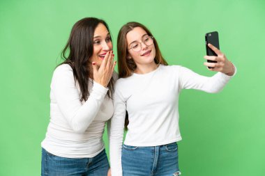 mother and daughter over isolated chroma key background making a selfie with the mobile