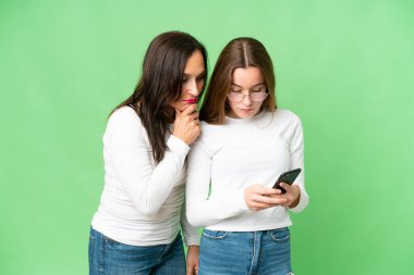 mother and daughter over isolated chroma key background reading a message with the mobile