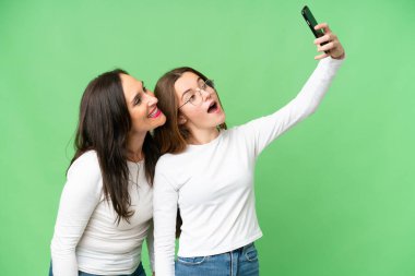 mother and daughter over isolated chroma key background making a selfie with the mobile