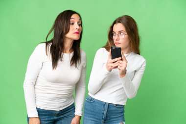 mother and daughter over isolated chroma key background reading a message with the mobile
