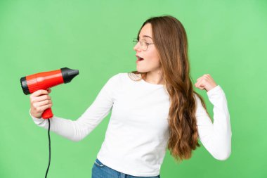Teenager girl holding a hairdryer over isolated chroma key background celebrating a victory