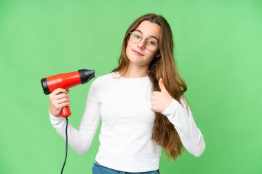 Teenager girl holding a hairdryer over isolated chroma key background with thumbs up because something good has happened