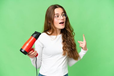 Teenager girl holding a hairdryer over isolated chroma key background intending to realizes the solution while lifting a finger up