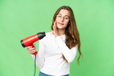 Teenager girl holding a hairdryer over isolated chroma key background whispering something