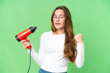 Teenager girl holding a hairdryer over isolated chroma key background celebrating a victory