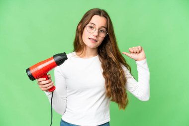 Teenager girl holding a hairdryer over isolated chroma key background proud and self-satisfied