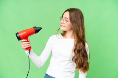 Teenager girl holding a hairdryer over isolated chroma key background with happy expression