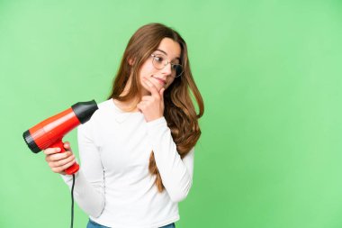 Teenager girl holding a hairdryer over isolated chroma key background thinking an idea and looking side