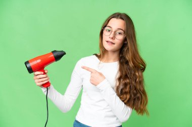 Teenager girl holding a hairdryer over isolated chroma key background and pointing it