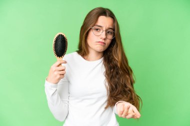 Teenager girl with hair comb over isolated chroma key background making doubts gesture while lifting the shoulders