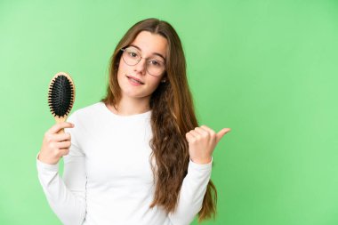 Teenager girl with hair comb over isolated chroma key background pointing to the side to present a product