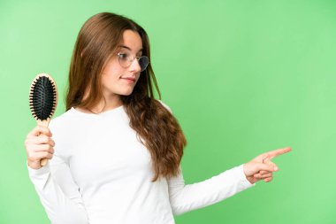 Teenager girl with hair comb over isolated chroma key background pointing to the side to present a product