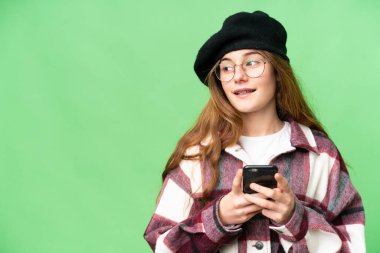 Teenager girl over isolated chroma key background using mobile phone and looking up