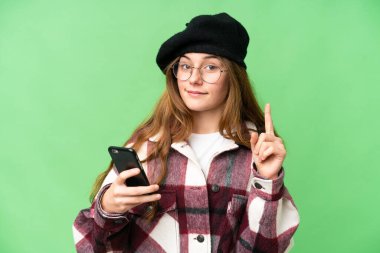 Teenager girl over isolated chroma key background using mobile phone and lifting finger