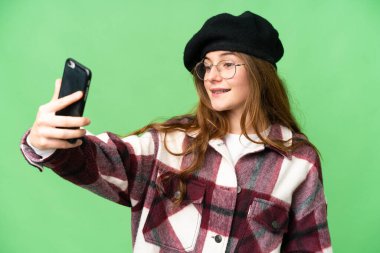 Teenager girl over isolated chroma key background making a selfie with mobile phone