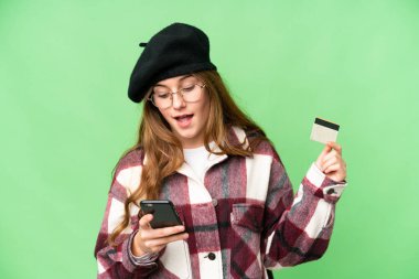 Teenager girl over isolated chroma key background buying with the mobile with a credit card