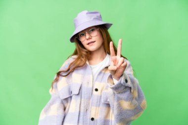 Teenager girl over isolated chroma key background smiling and showing victory sign